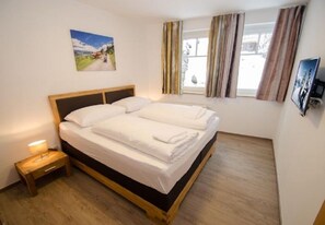 A bedroom with a double bed, a bedside table with a lamp, a window with curtains, and a painting on the wall. - Apartment Summer & Winter Fun II (Zell am See)