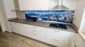 A modern kitchen with white cabinets, a stainless steel range hood, and a backsplash depicting a snowy mountain landscape. - Apartment Summer & Winter Fun II (Zell am See)