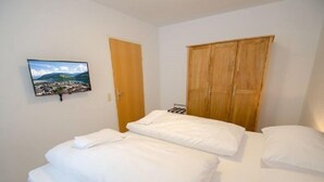 A bedroom with two beds, a wooden wardrobe, and a television on the wall. - Apartment Summer & Winter Fun II (Zell am See)