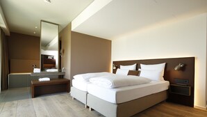 A modern hotel room with a large bed, a bedside table, a nightstand, a mirror, and a bathroom with a bathtub and sink. - Das ACKER Hotel (Neuburg)