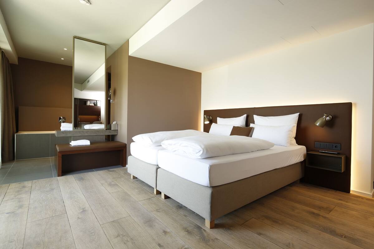 Une chambre d’hôtel moderne dotée d’un grand lit, d’une table de chevet, d’une commode, d’un miroir et d’une salle de bain avec une baignoire et un lavabo.