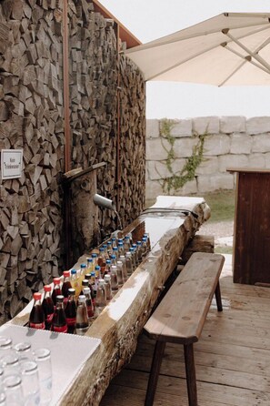 An outdoor bar area with a long wooden bench and a table filled with bottles and glasses. - Das ACKER Hotel (Neuburg)