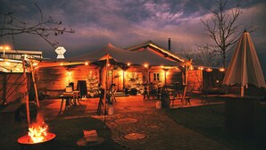 A rustic wooden building with a covered patio area, outdoor seating, and a fire pit. - Das ACKER Hotel (Neuburg)