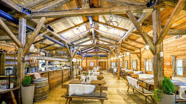 A rustic wooden interior with high ceilings, wooden beams, and a bar area with shelves of glasses and bottles. - Das ACKER Hotel (Neuburg)