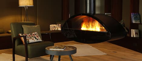 Una sala de estar acogedora con una chimenea moderna, un sofá cómodo, una mesita auxiliar pequeña y una estantería llena de libros.