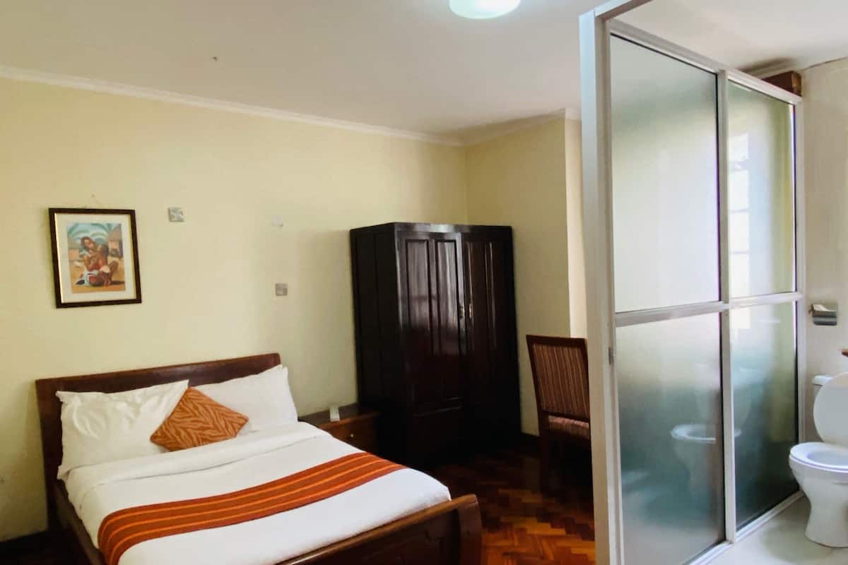 A hotel room with a bed, a wardrobe, a chair, and a toilet.