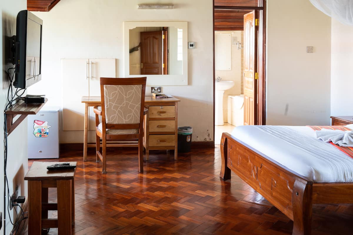 A bedroom with a wooden bed, a desk with a chair, a mirror, and a small refrigerator.