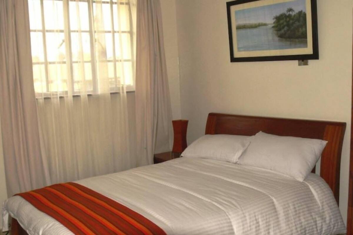 A bedroom with a bed, a window with curtains, and a framed picture on the wall.