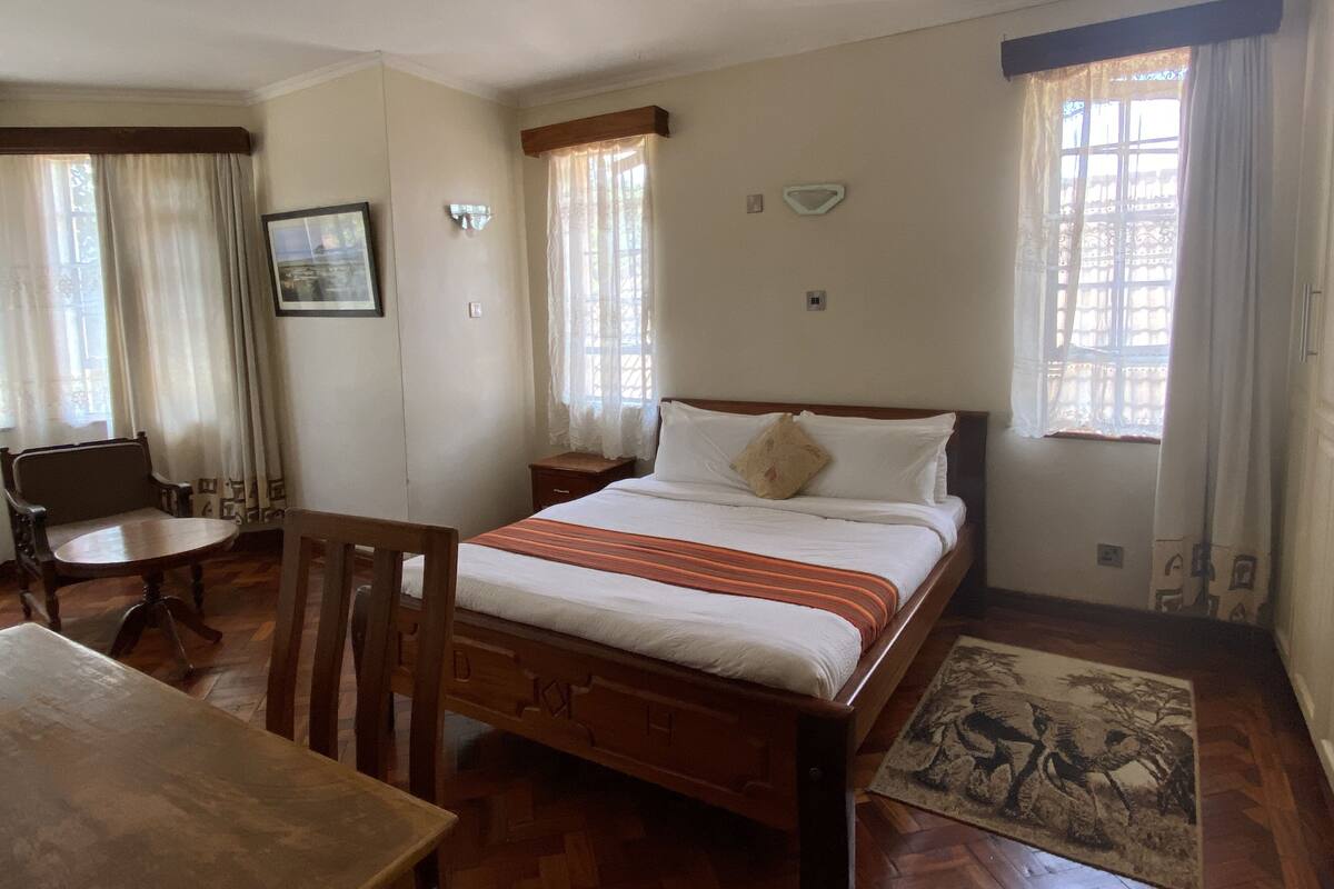 A bedroom with a wooden bed, a wooden chair, a small bedside table, and a window with curtains.