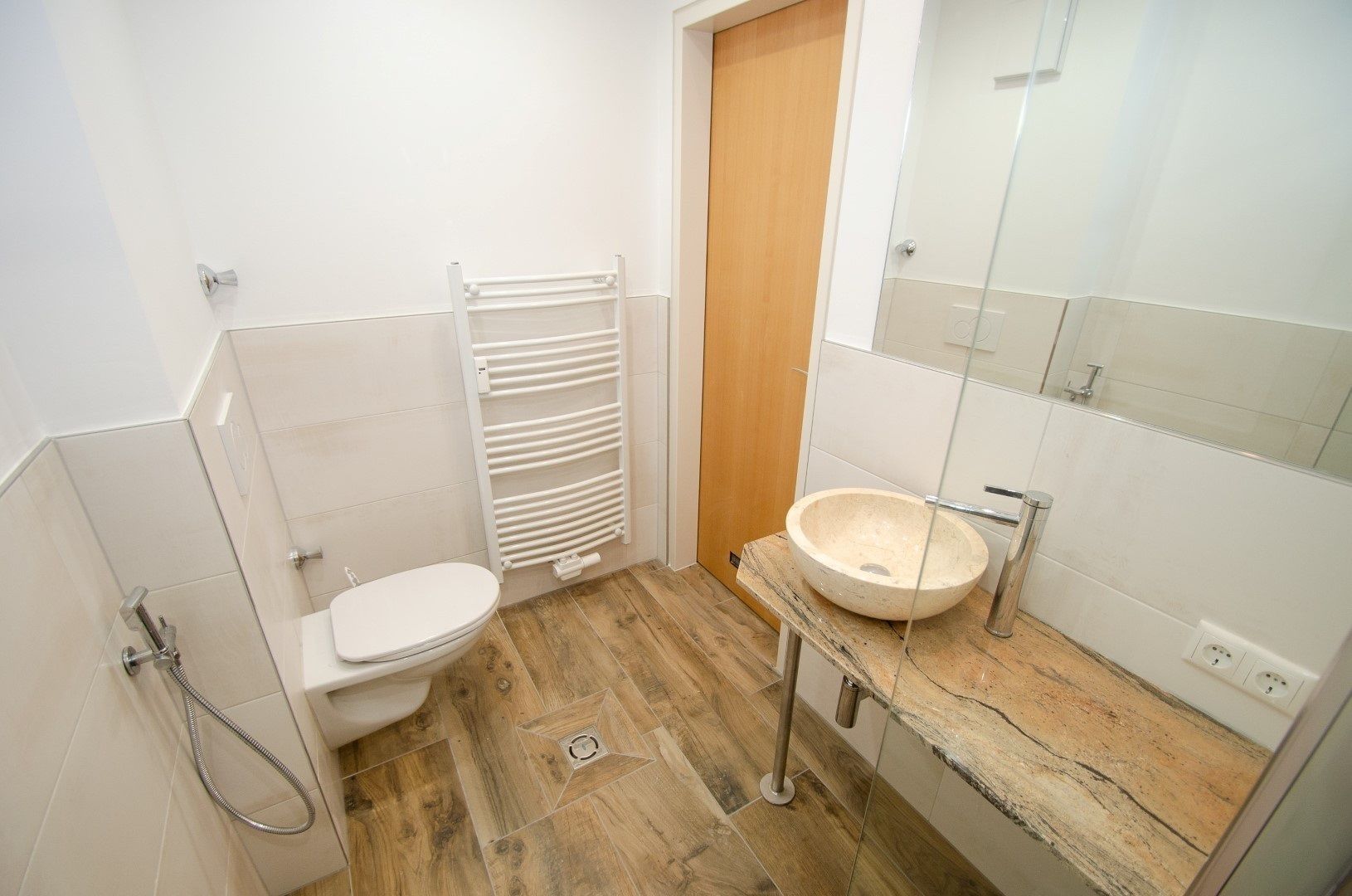 Ein kleines Badezimmer mit Toilette, einem weißen Waschbecken und Holzboden.