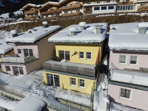En grupp av höga byggnader med flera våningar, balkonger och snötäckta tak, med ett bergigt landskap i bakgrunden.