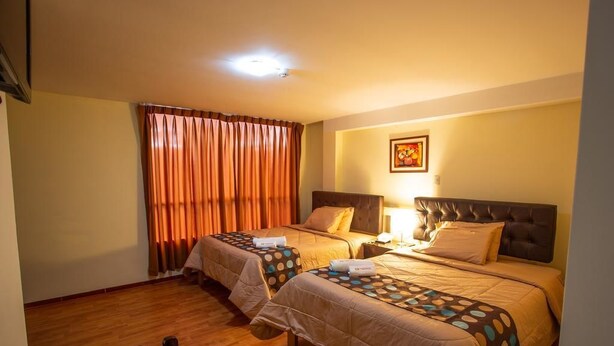 A hotel room with two beds, a wooden floor, a window with curtains, and a framed picture on the wall. - Hotel Santa Beatriz (Cusco)