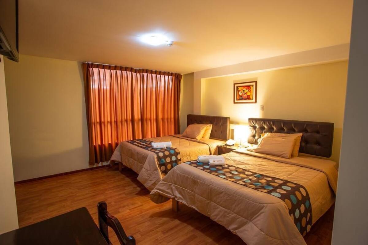 A hotel room with two beds, a wooden floor, a window with curtains, and a framed picture on the wall.