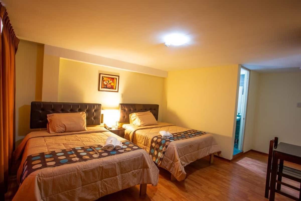 A hotel room with two beds, a nightstand, a lamp, and a framed picture on the wall.