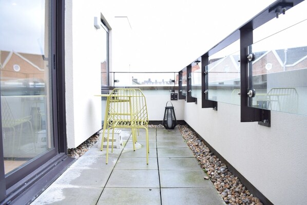 A narrow outdoor corridor with a yellow chair, a lantern, and a glass railing.