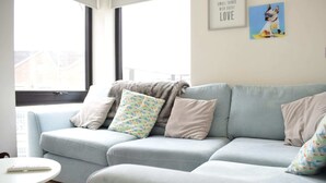 Ein modernes Wohnzimmer mit einem hellblauen Sofa, einem kleinen runden Tisch und einem Fenster mit Blick auf Gebäude.