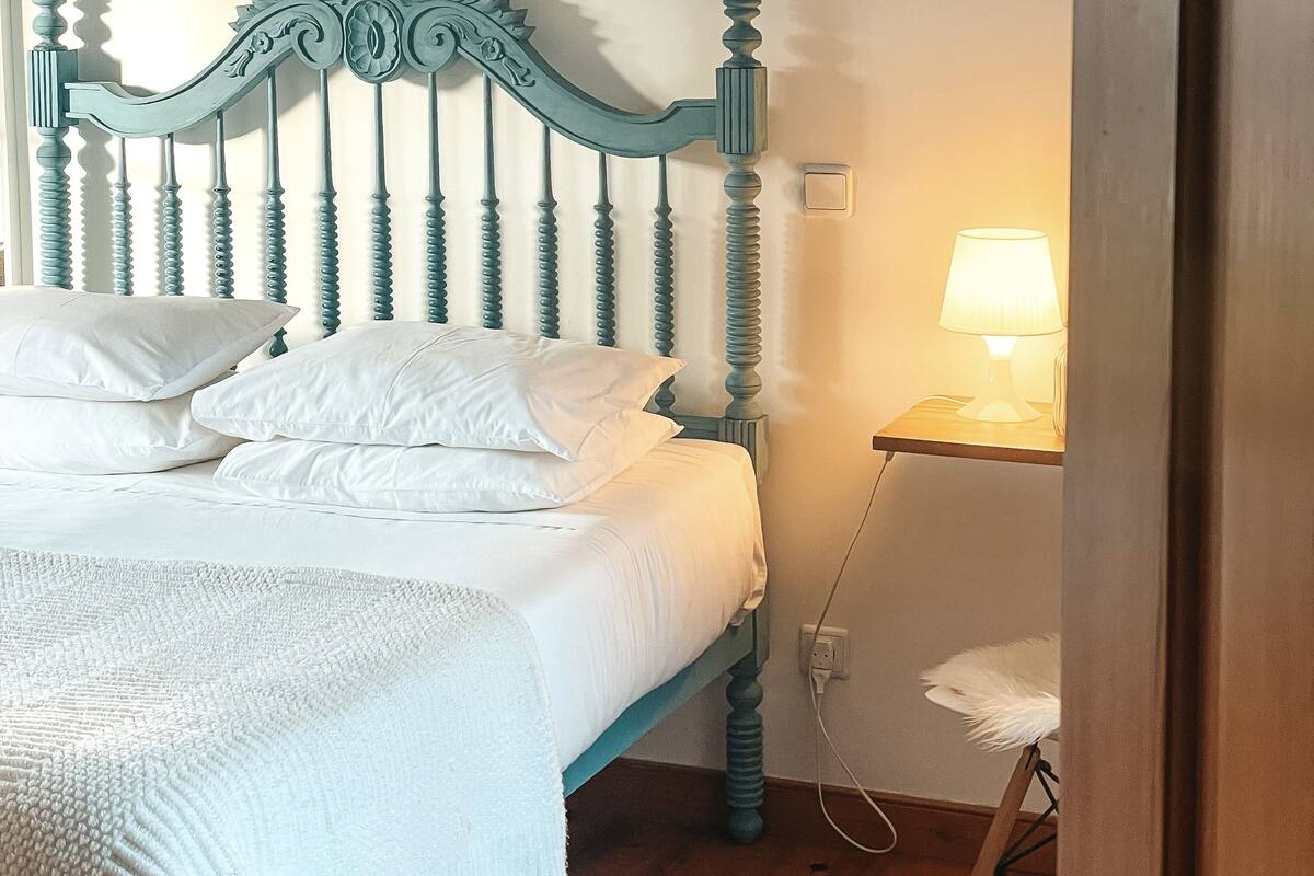 A bed with a wooden headboard, white bedding, and a bedside table with a lamp.