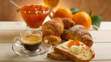 Un desayuno con cruasanes, tostadas con mantequilla, una taza de café y un bol de mermelada.