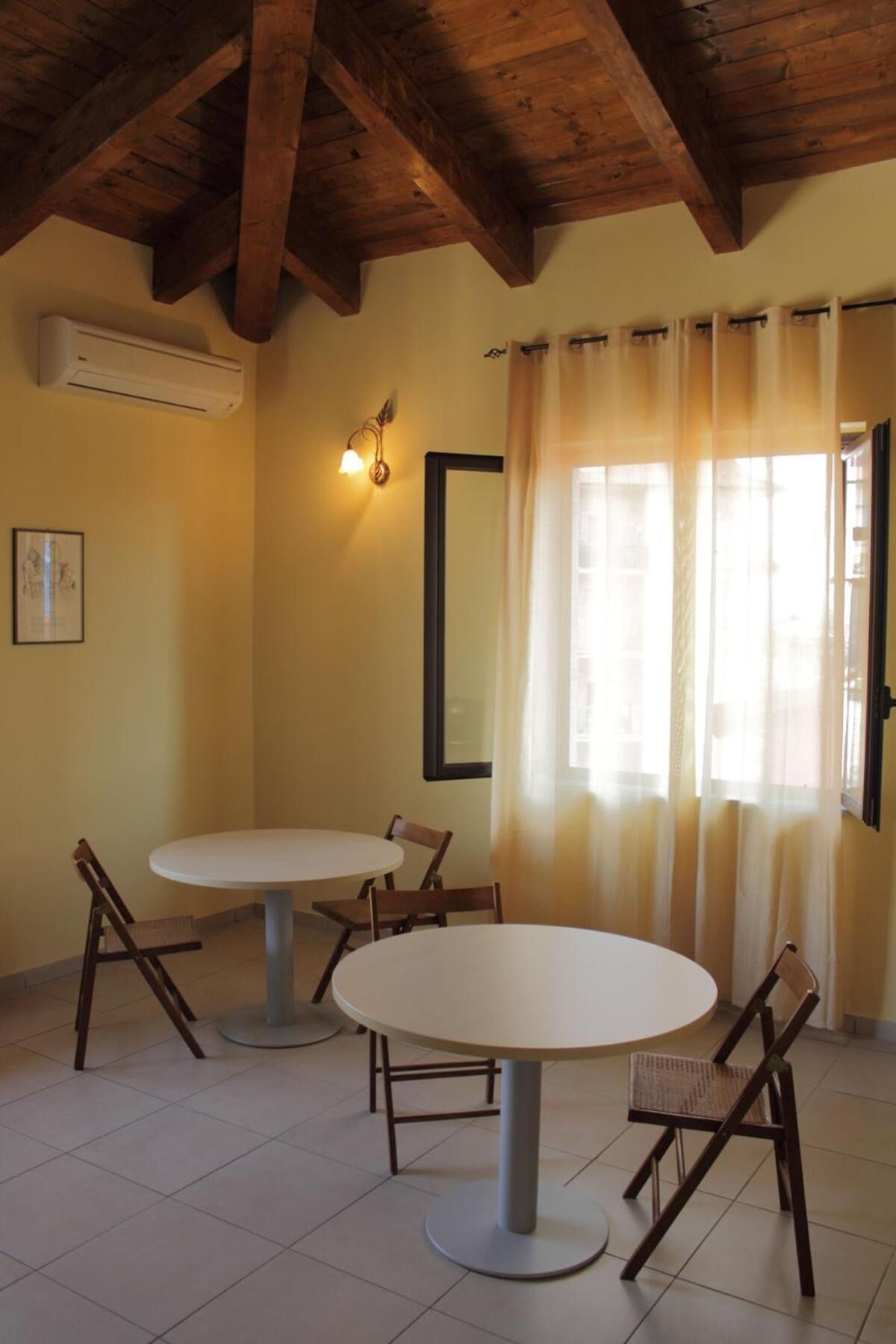 Una habitación con una mesa redonda y sillas, un ventilador de techo, un aire acondicionado instalado en la pared y una ventana con cortinas.
