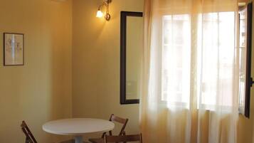 Una habitación con una mesa redonda y sillas, un ventilador de techo, un aire acondicionado instalado en la pared y una ventana con cortinas.