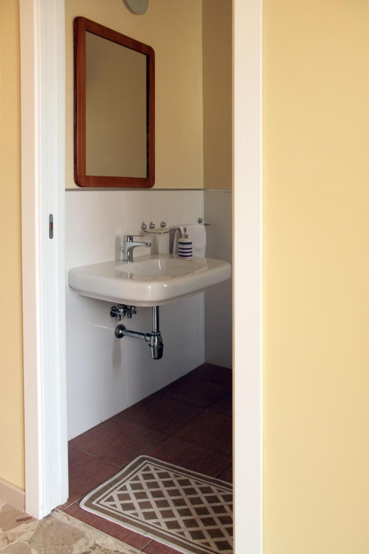 A bathroom with a white sink, a mirror above it, and a patterned mat on the floor.