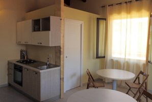 Cocina compacta con estufa, lavamanos y armarios, una puerta blanca y un comedor con mesa y sillas.