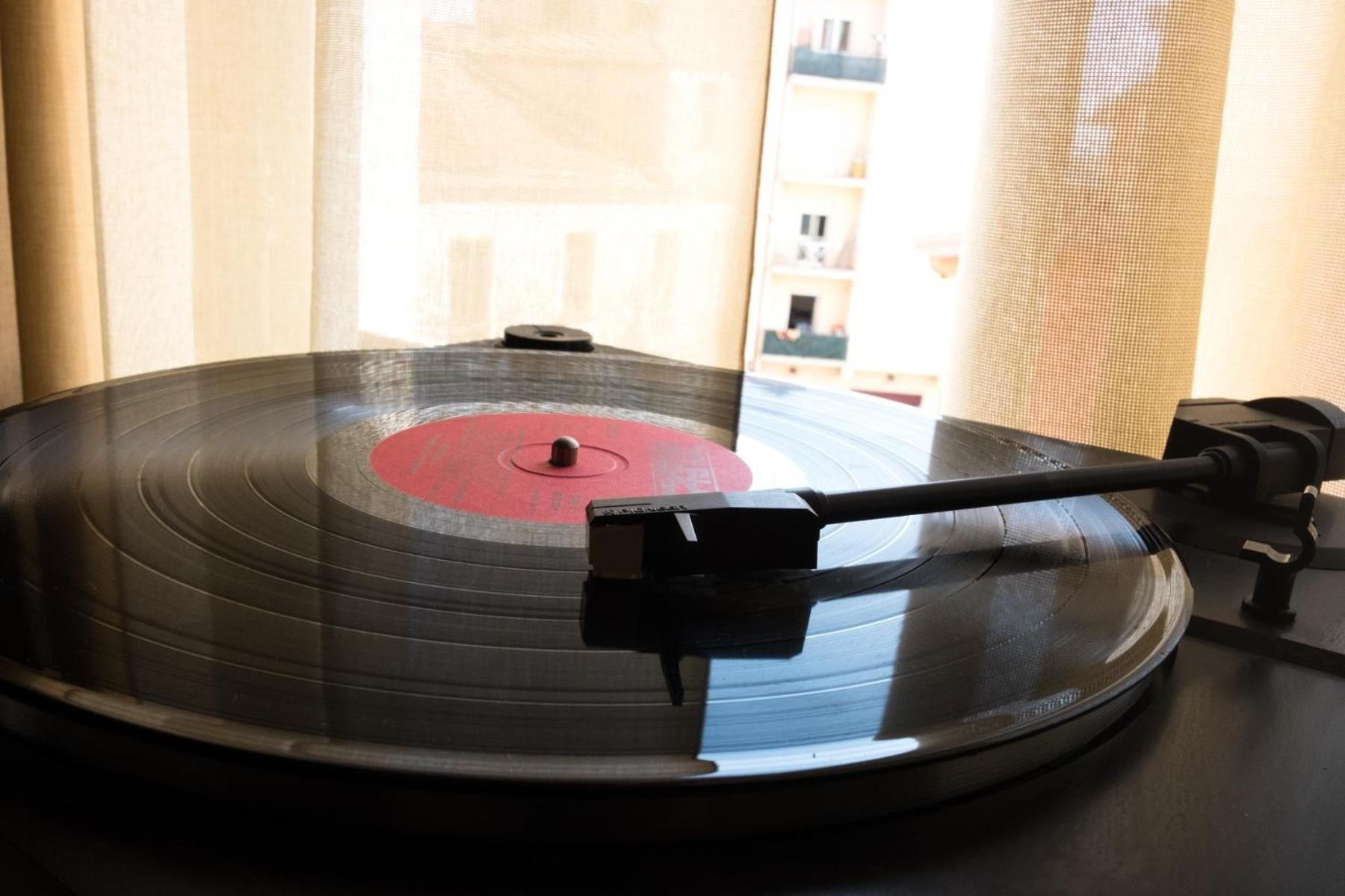 A vinyl record on a turntable with a needle, positioned near a window with curtains.