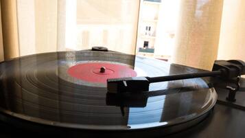 A vinyl record on a turntable with a needle, positioned near a window with curtains.