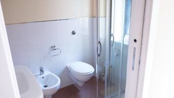 Un baño con bidé, inodoro y cabina de ducha de vidrio.