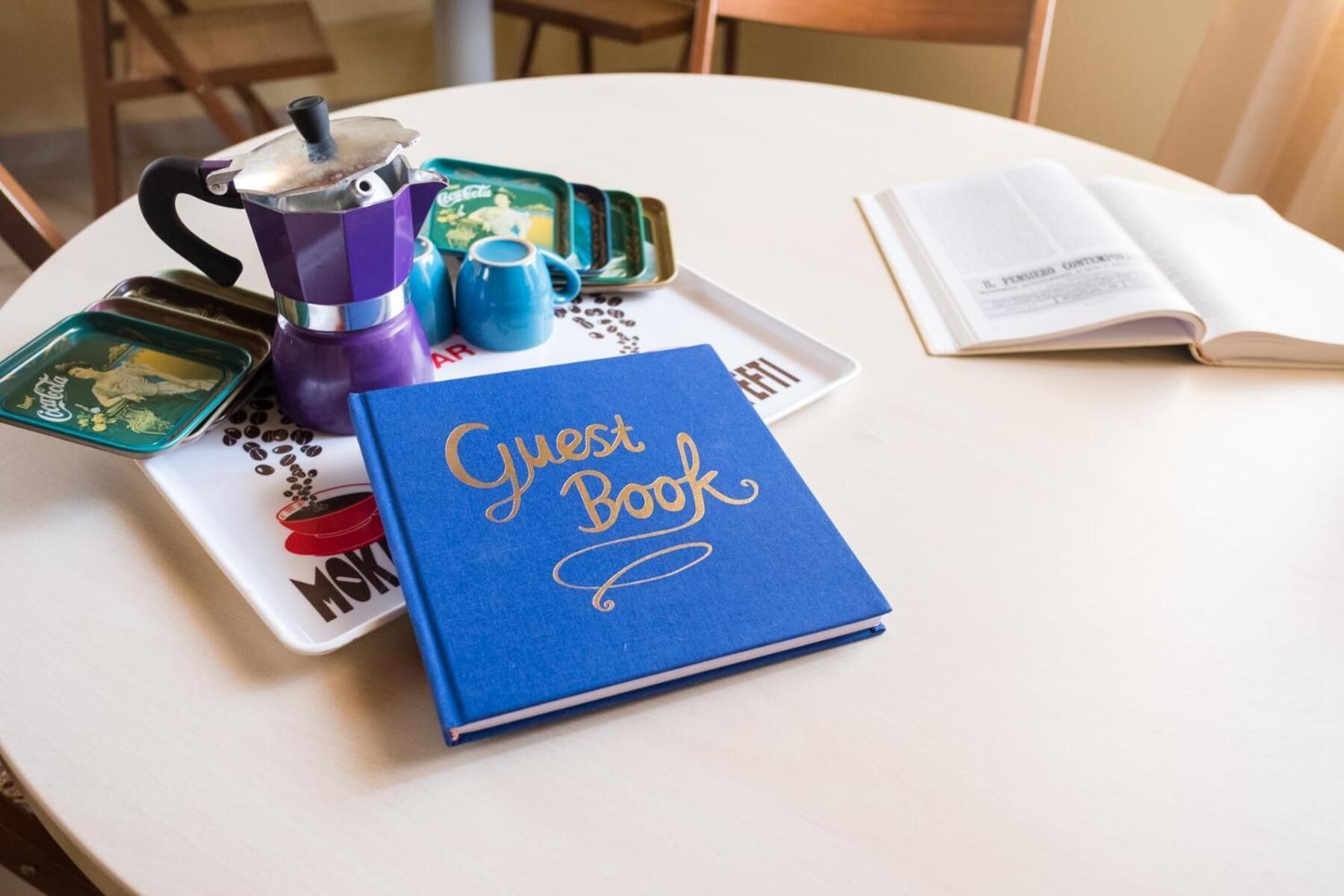 A table with a blue guest book, a coffee pot, and a tray with coffee cups and a mug.