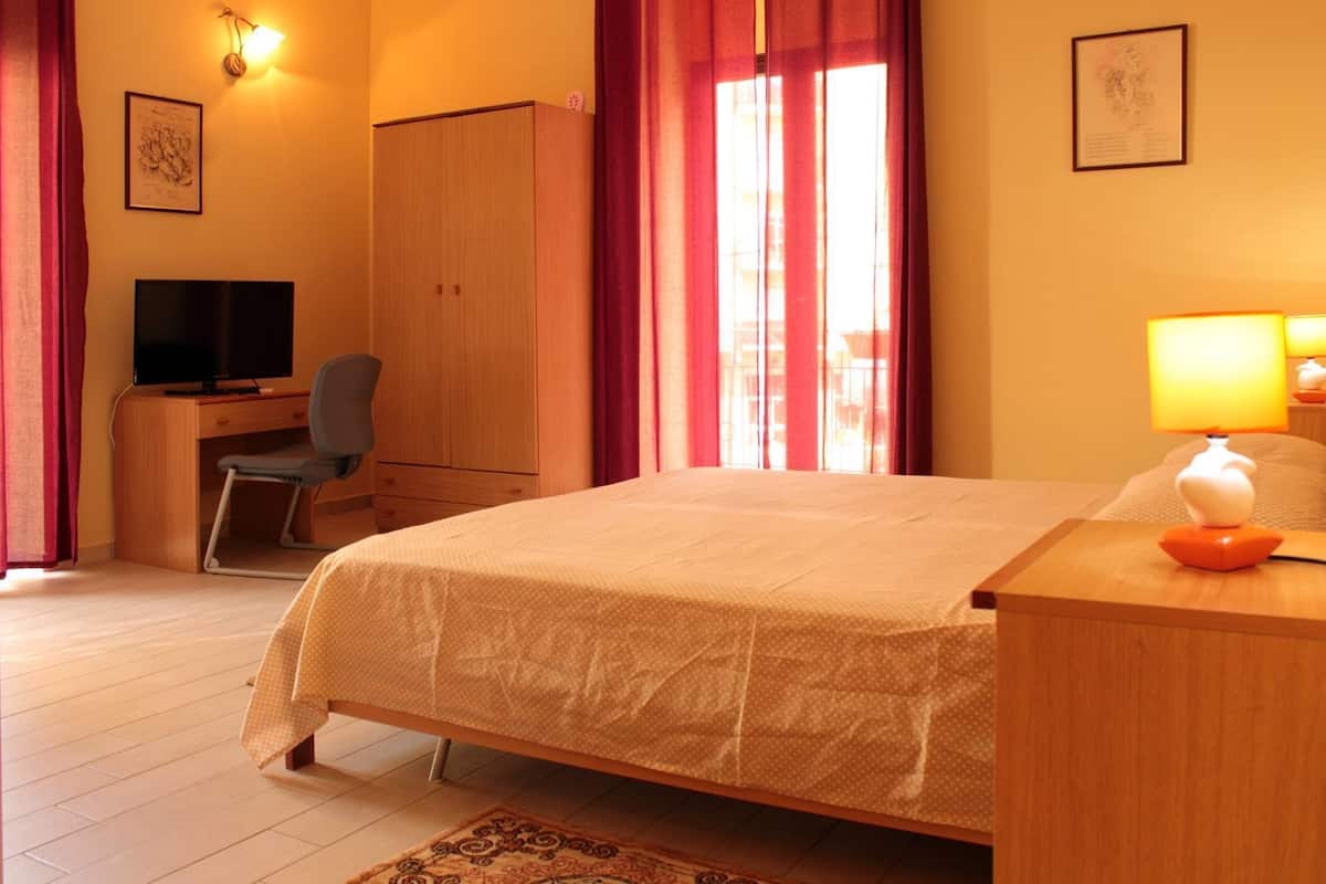 Una camera d'hotel con un letto, una scrivania con una sedia, una televisione e una lampada.