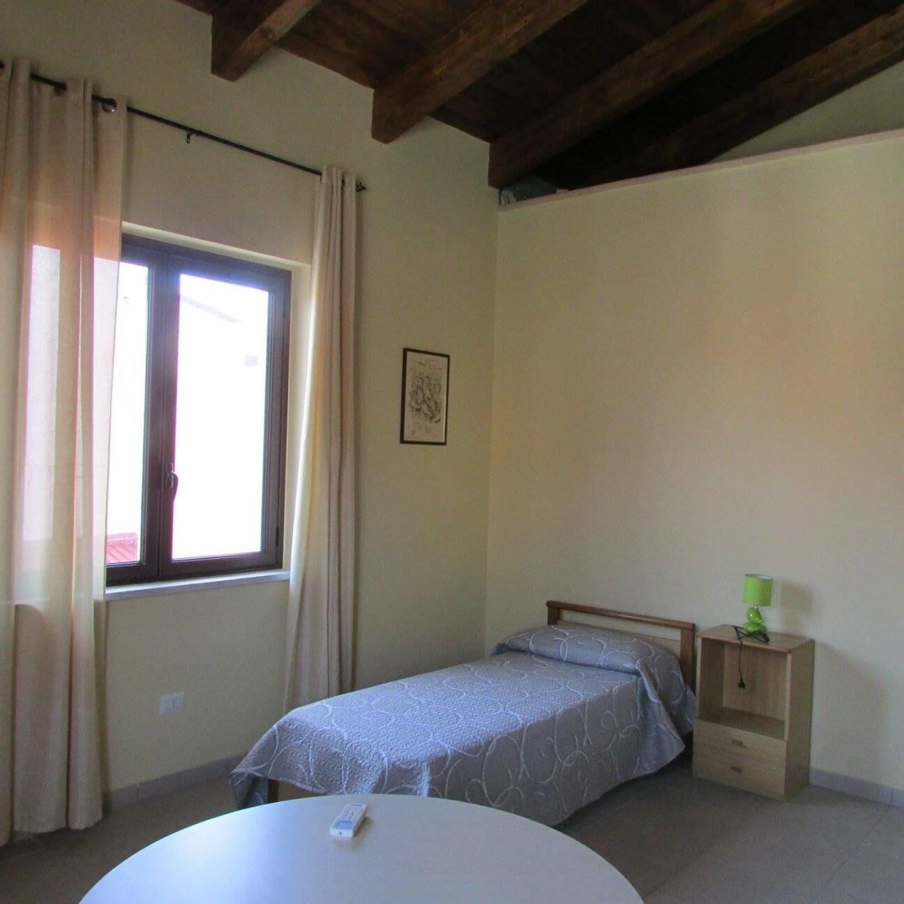 A small, simple room with a single bed, a small table, and a window with curtains.