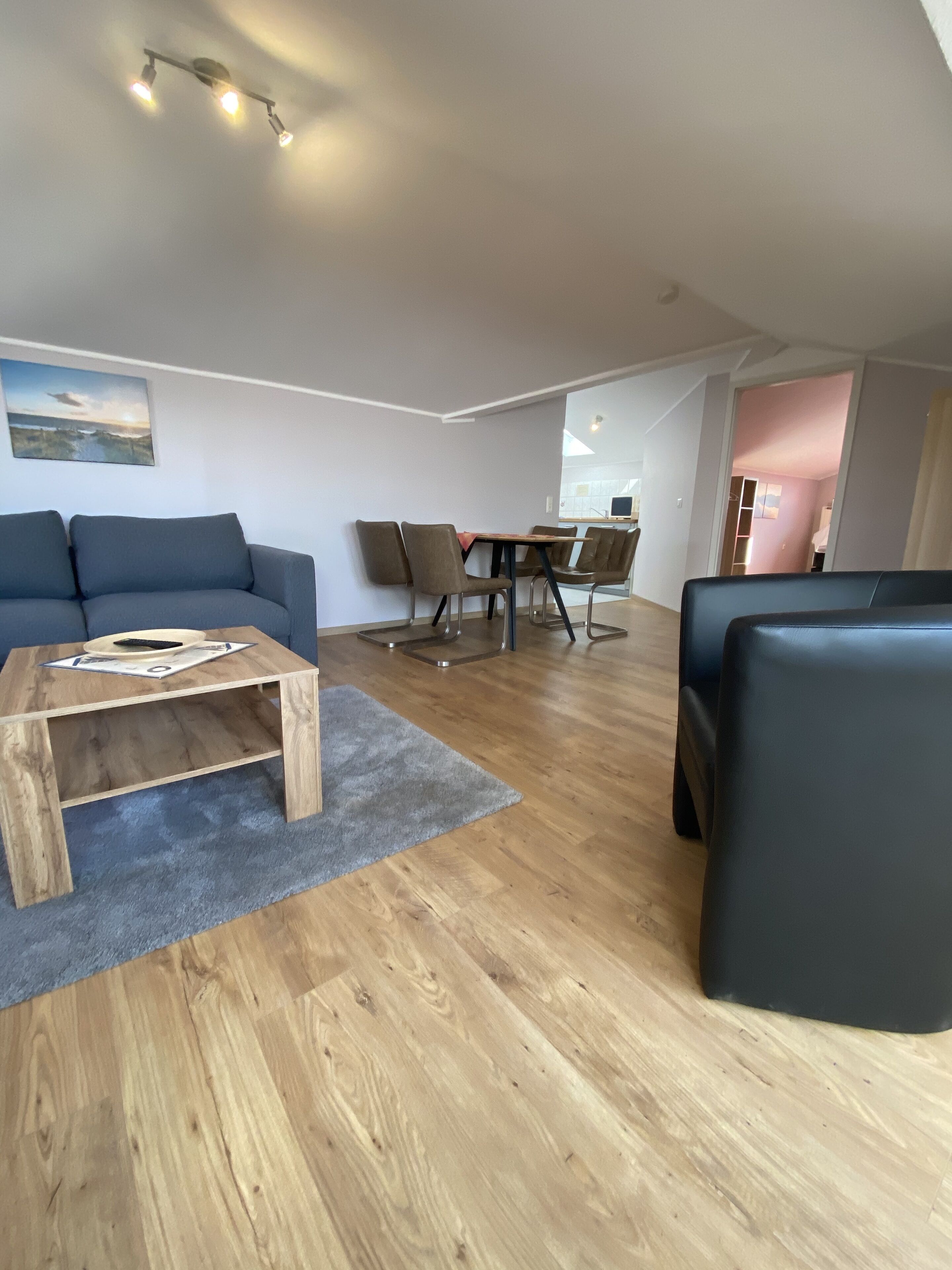 A modern living room with a wooden coffee table, a blue sofa, and a dining area with chairs and a table.