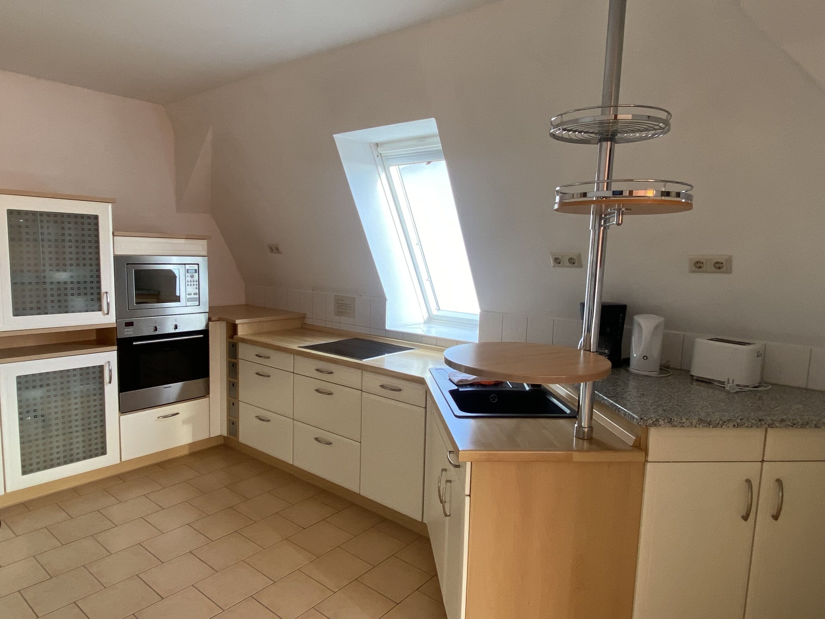 A compact kitchen with a microwave, oven, sink, and a small window.