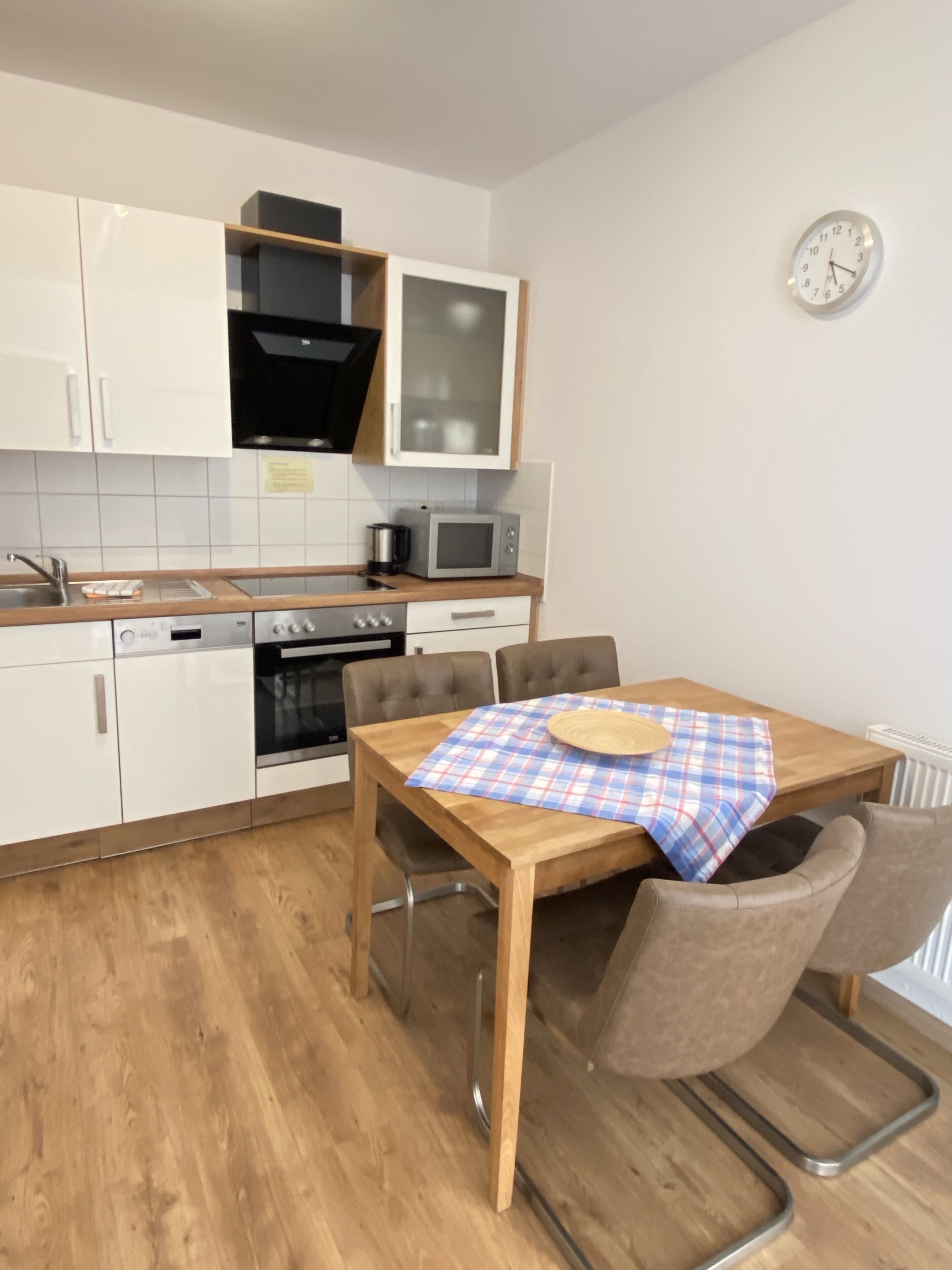 Een moderne keuken met witte kasten, een magnetron, een oven en een eettafel met stoelen.