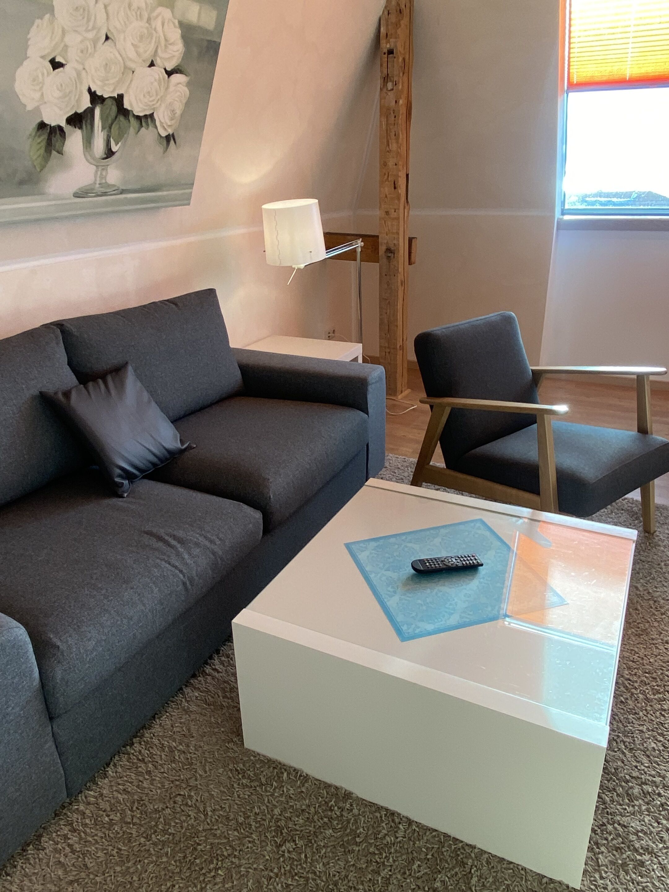 En moderne stue med en grå sofa, en matchende lænestol og et hvidt sofabord med en fjernbetjening på.