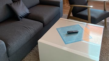 En moderne stue med en grå sofa, en matchende lænestol og et hvidt sofabord med en fjernbetjening på.