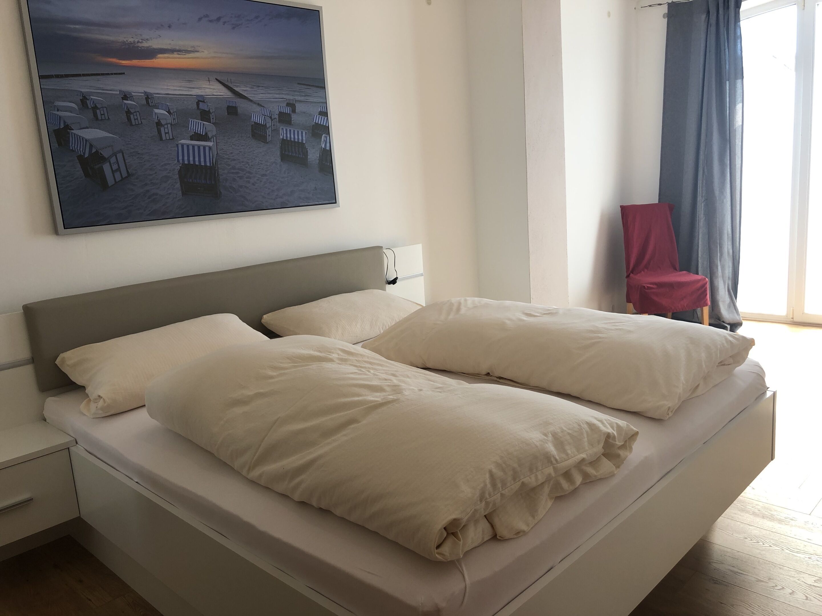 A bed with two pillows, a nightstand, a wall-mounted power outlet, and a window with curtains.