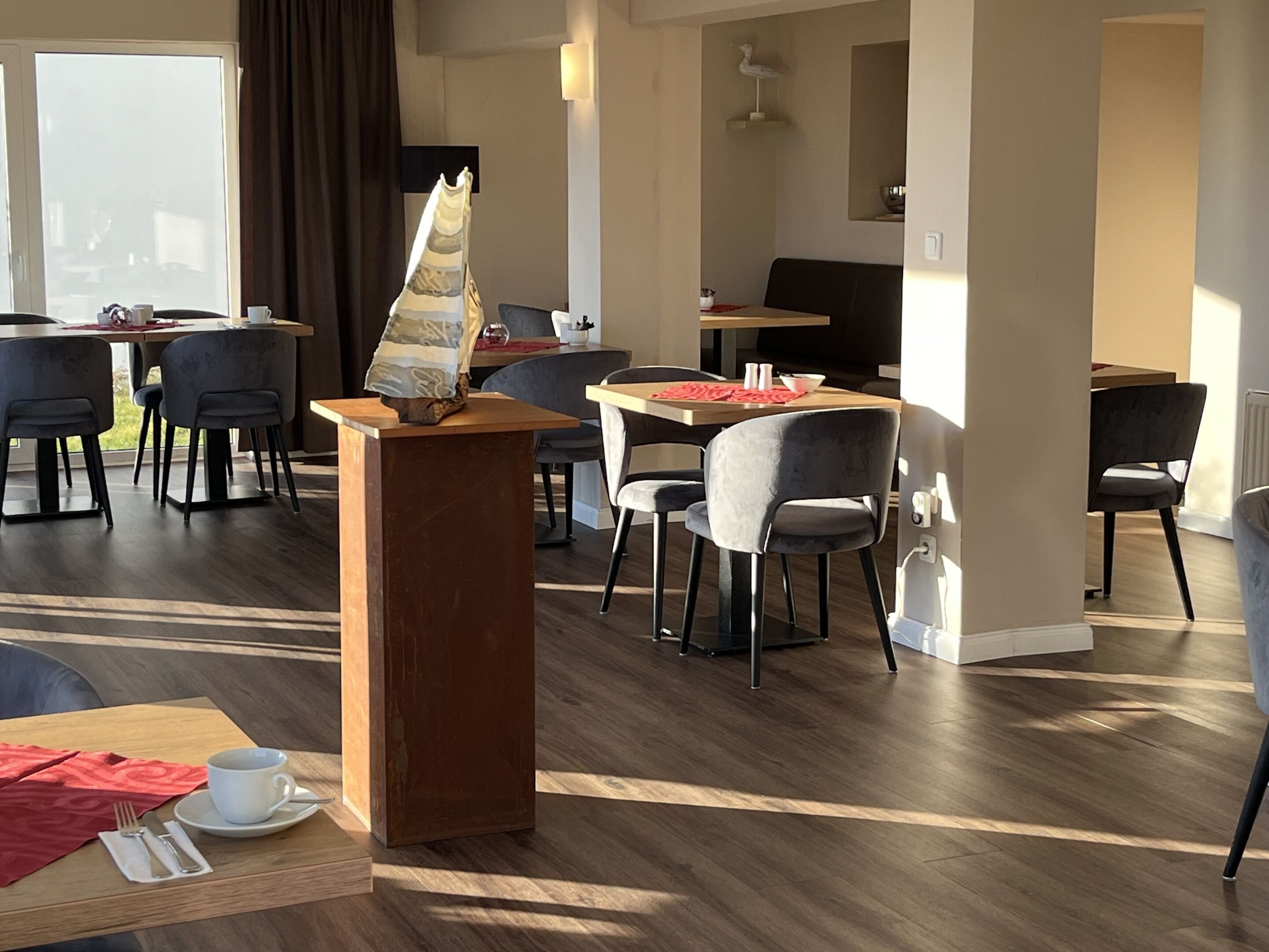A modern dining area with wooden tables and chairs, a central podium with a menu, and a large window providing natural light.