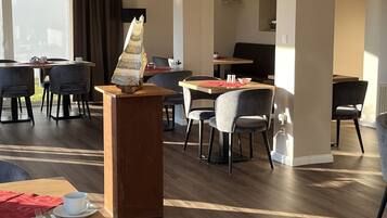Un espace de restauration moderne avec des tables et des chaises en bois, un podium central où est présenté le menu, et une grande fenêtre qui laisse entrer la lumière naturelle.