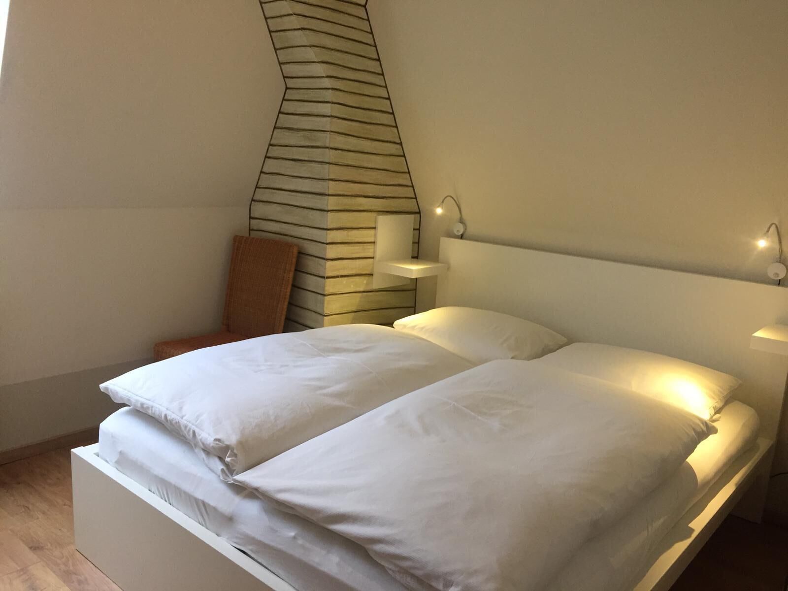 A double bed with white linens in a modern room with a unique curved wall design and wall-mounted reading lights.