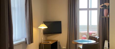 Habitación de hotel con cama, escritorio, silla, televisor y ventana con cortinas.
