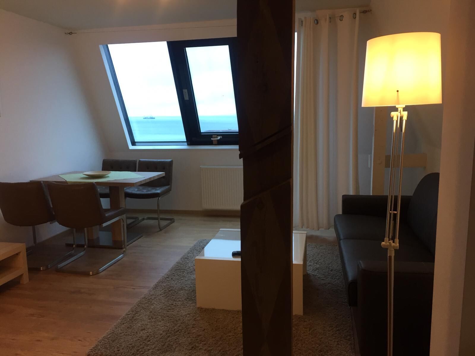 A modern living room with a dining area, a large window with a view, and a floor lamp.