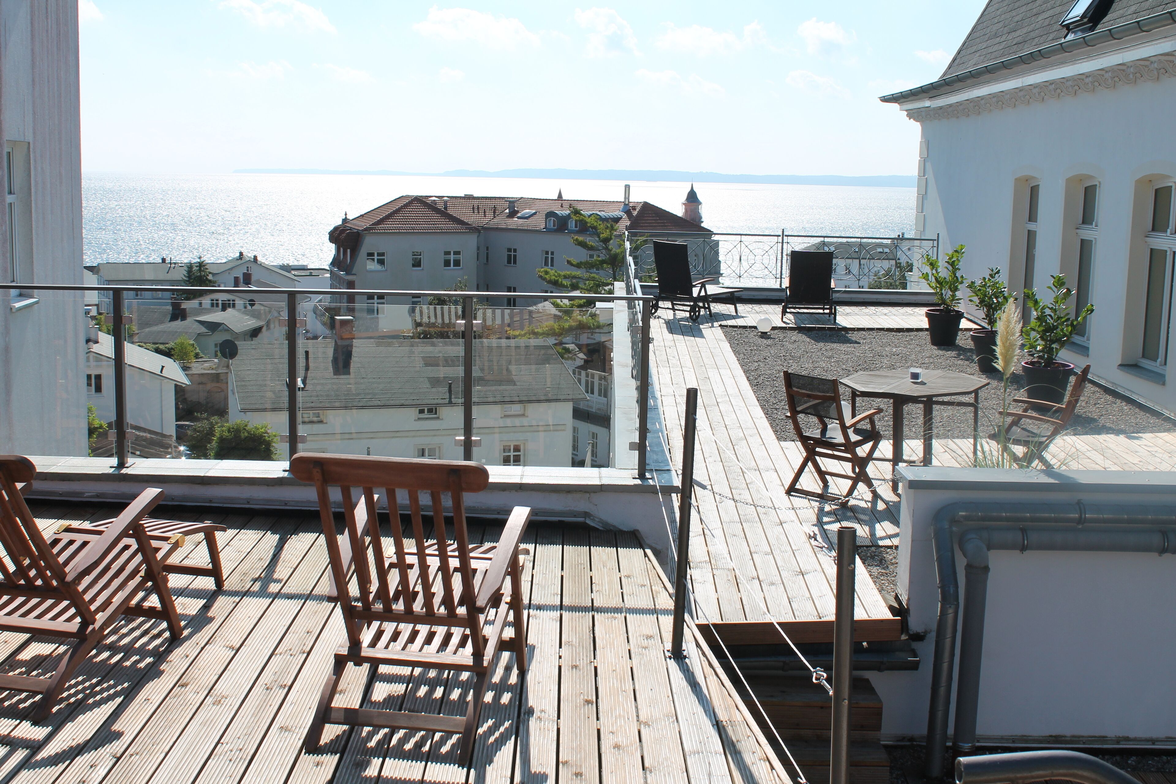 Eine Holzterrasse mit Stühlen und einem Tisch, mit Blick auf ein Gewässer und Gebäude.