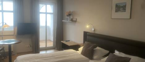A hotel room with a bed, a desk, a chair, a lamp, and a picture on the wall.