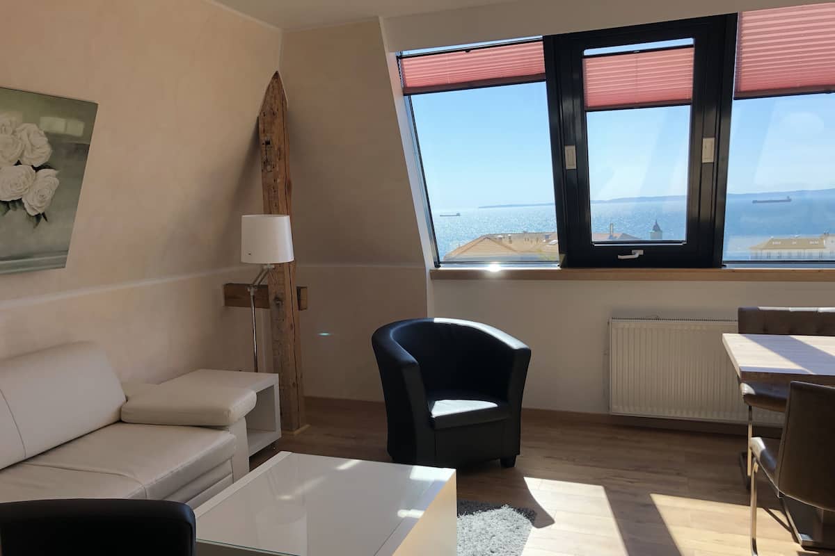 Un salon moderne avec un canapé, une table basse, un fauteuil et une vue sur la mer grâce à de grandes fenêtres.