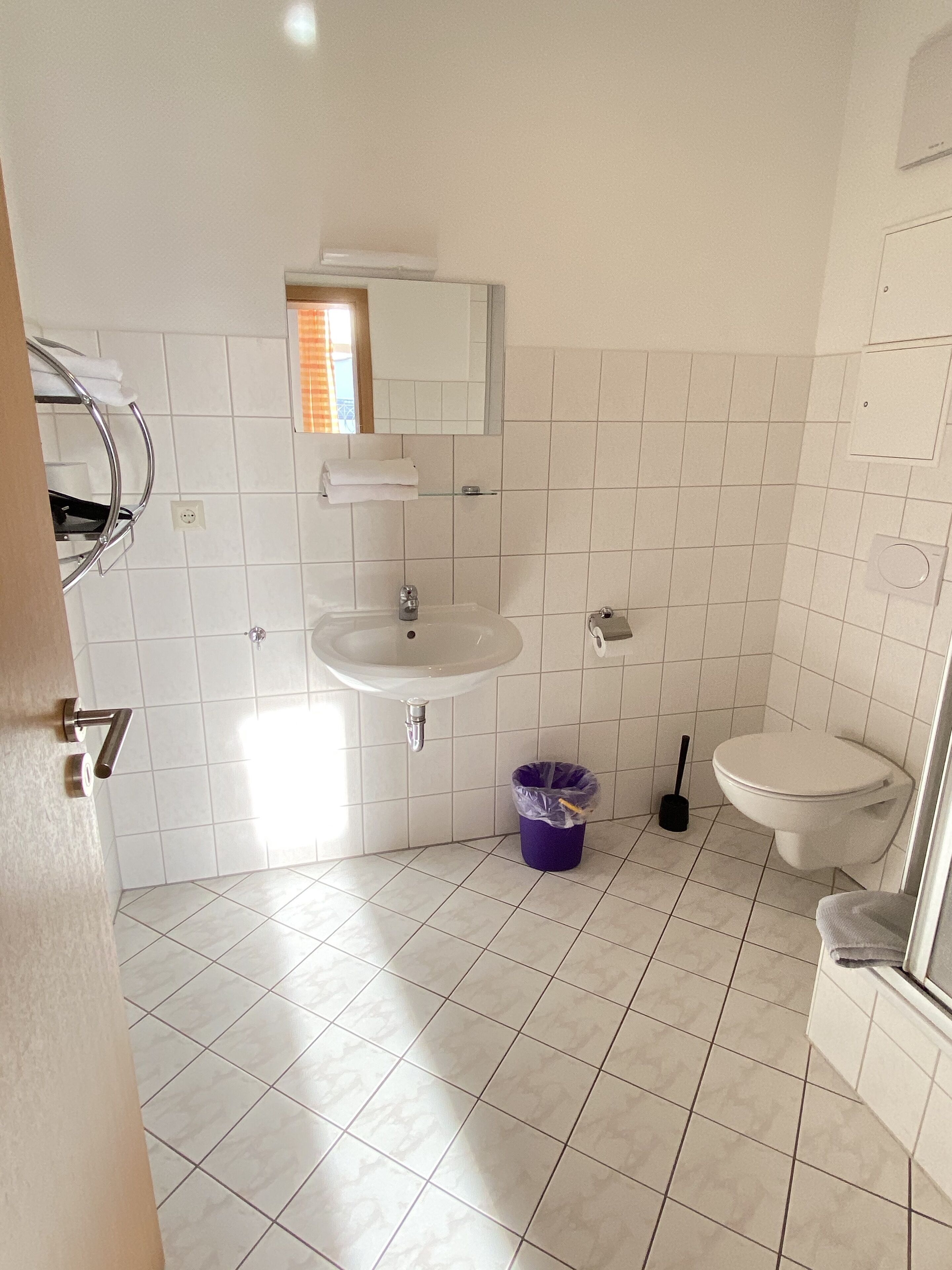 Un bagno con piastrelle bianche, un lavandino, un water e un cestino.