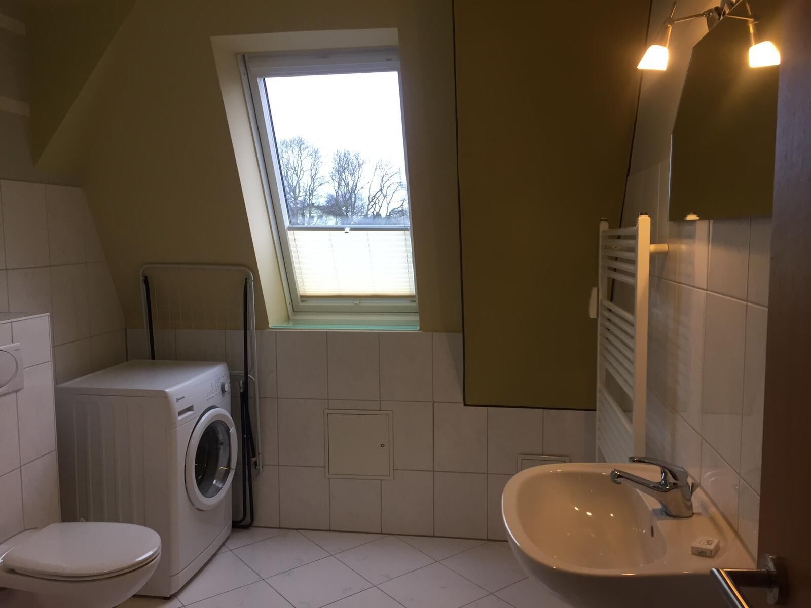 A compact bathroom with a washing machine, toilet, and sink. A skylight provides natural light.