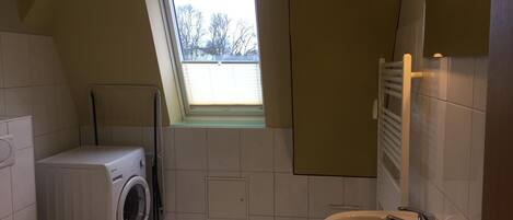 A compact bathroom with a washing machine, toilet, and sink. A skylight provides natural light.