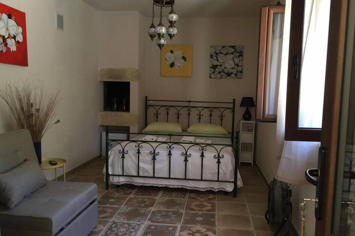 A bedroom with a bed, a chair, a bedside table, a lamp, and a window.